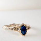Anillo de oro amarillo 10k con zafiro de Montana y dos diamantes de laboratorio engastados en una banda orgánica esculpida, visto de frente sobre fondo blanco.