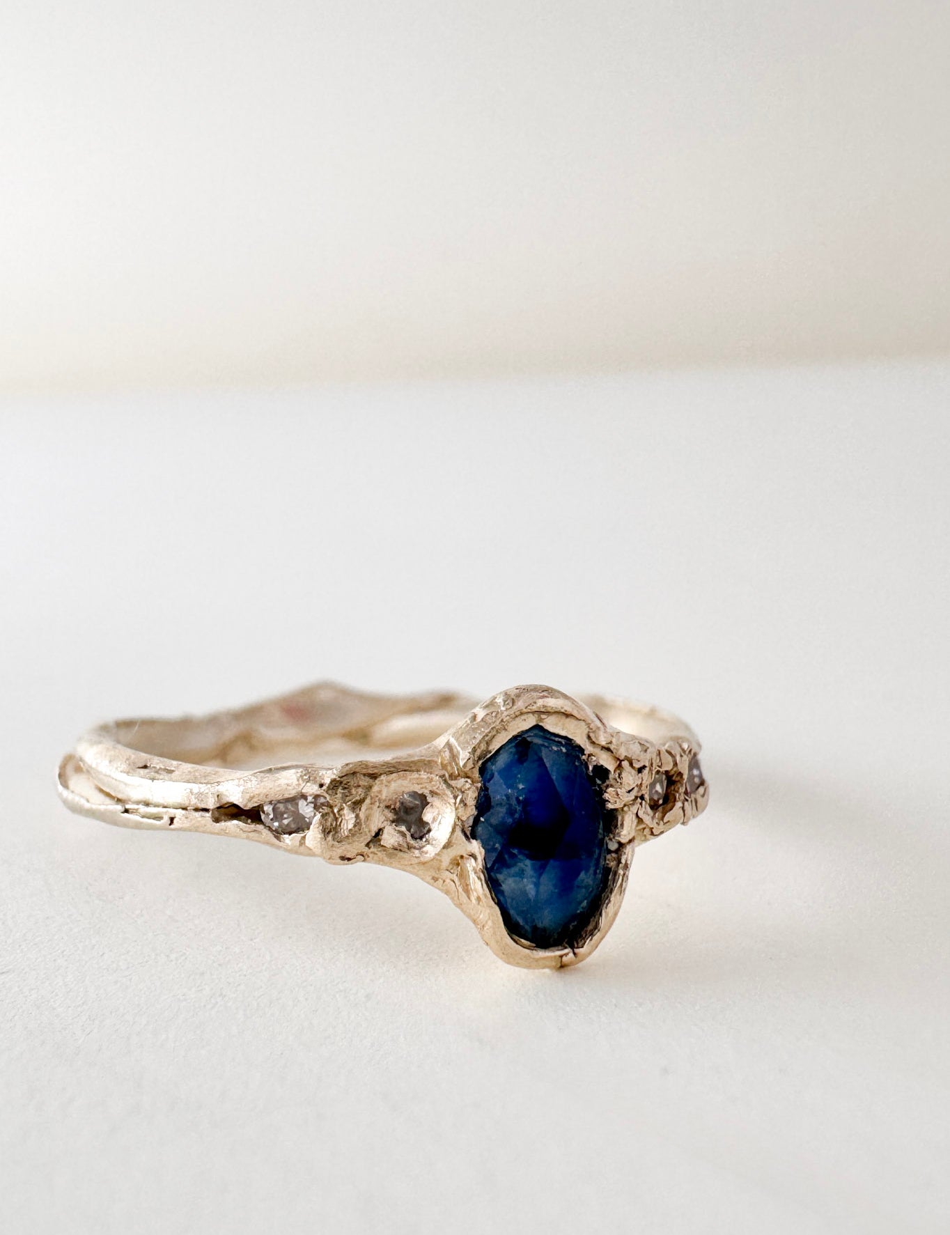 Anillo de oro amarillo 10k con zafiro de Montana y dos diamantes de laboratorio engastados en una banda orgánica esculpida, visto de frente sobre fondo blanco.