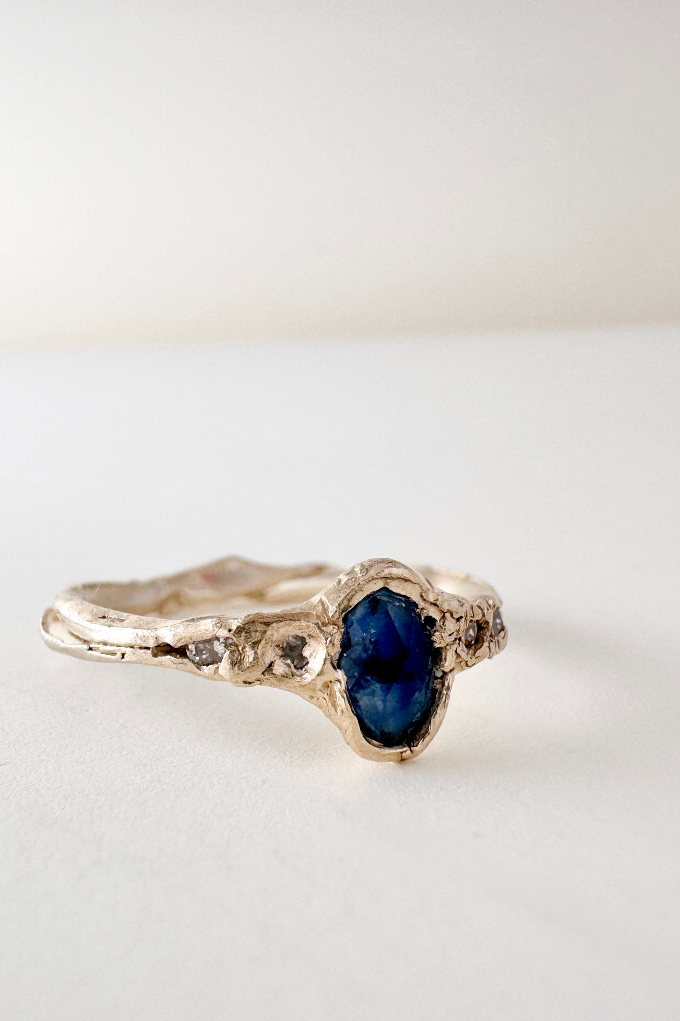 Anillo de oro amarillo 10k con zafiro de Montana y dos diamantes de laboratorio engastados en una banda orgánica esculpida, visto de frente sobre fondo blanco.