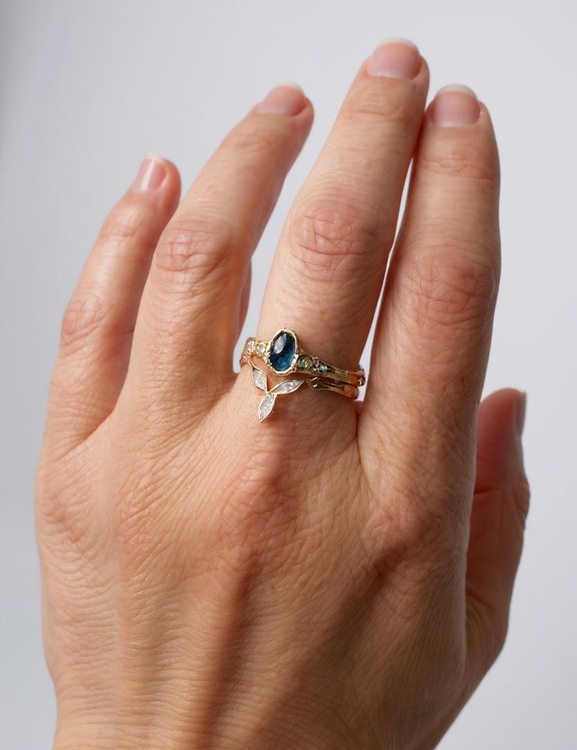 Anillo con zafiro de Montana y diamantes de laboratorio en oro amarillo 10k puesto en una mano, fotografiado sobre fondo neutro claro.