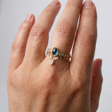 Anillo con zafiro de Montana y diamantes de laboratorio en oro amarillo 10k puesto en una mano, fotografiado sobre fondo neutro claro.