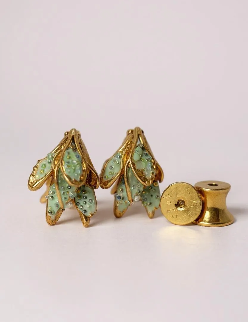 Disposición plana de dos aretes Topos Nebula Mini en forma de hoja pintados a mano en verde con granulación de vidrio, acompañados de un topo redondo de bronce bañado en oro colocado aparte, sobre superficie blanca.