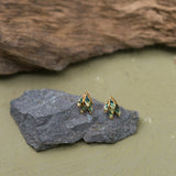 Dos topos Nebula Mini en forma de hoja con montura en bronce bañado en oro, pintados a mano en verde  y con granulación de vidrio, reposando sobre una piedra gris sobre fondo oliva.