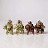 Disposición plana de cuatro aretes Topos Nebula Mini en forma de hoja alineados sobre fondo blanco: dos pintados a mano en verde y dos en rust, cada uno con granulación de vidrio y montura de bronce bañado en oro.