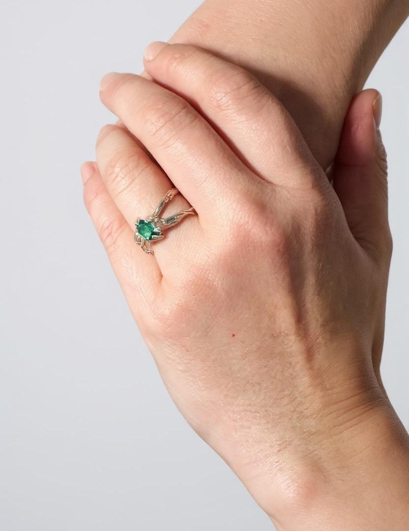 Anillo de plata con esmeralda de laboratorio puesto en una mano, fotografiado frente a una pared gris clara.