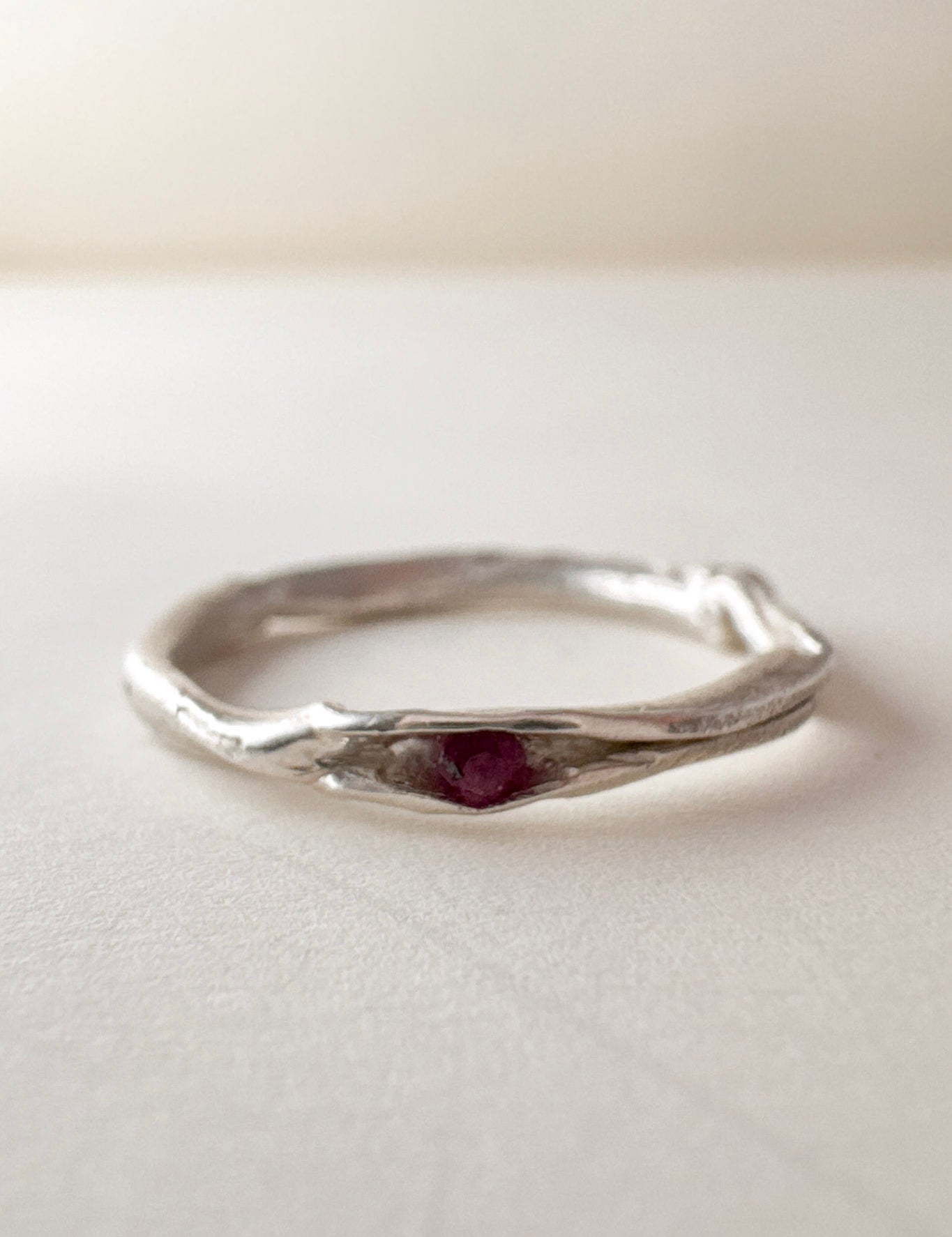 vista frontal de anillo nido, fabricado en plata con un rubí en el centro, sobre fondo claro