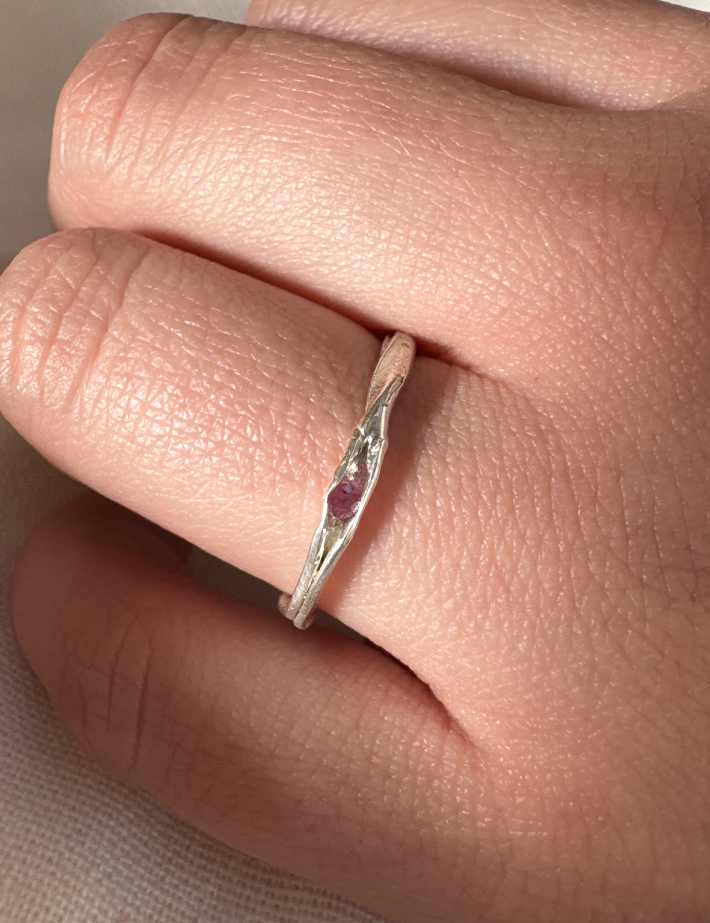 Anillo de plata con una piedra preciosa roja en un dedo sobre un fondo neutro.