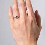 Anillo de plata esterlina con piedra del sol puesto en una mano, fotografiado sobre fondo gris claro.