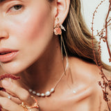 Topos Rosa Salvaje en bronce bañado en oro con granulación coral, usados por modelo entre follaje seco, en plano cerrado del rostro.