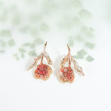 Topos Rosa Salvaje en bronce bañado en oro con pétalos coral, fotografiados sobre fondo blanco con sombras botánicas suaves.