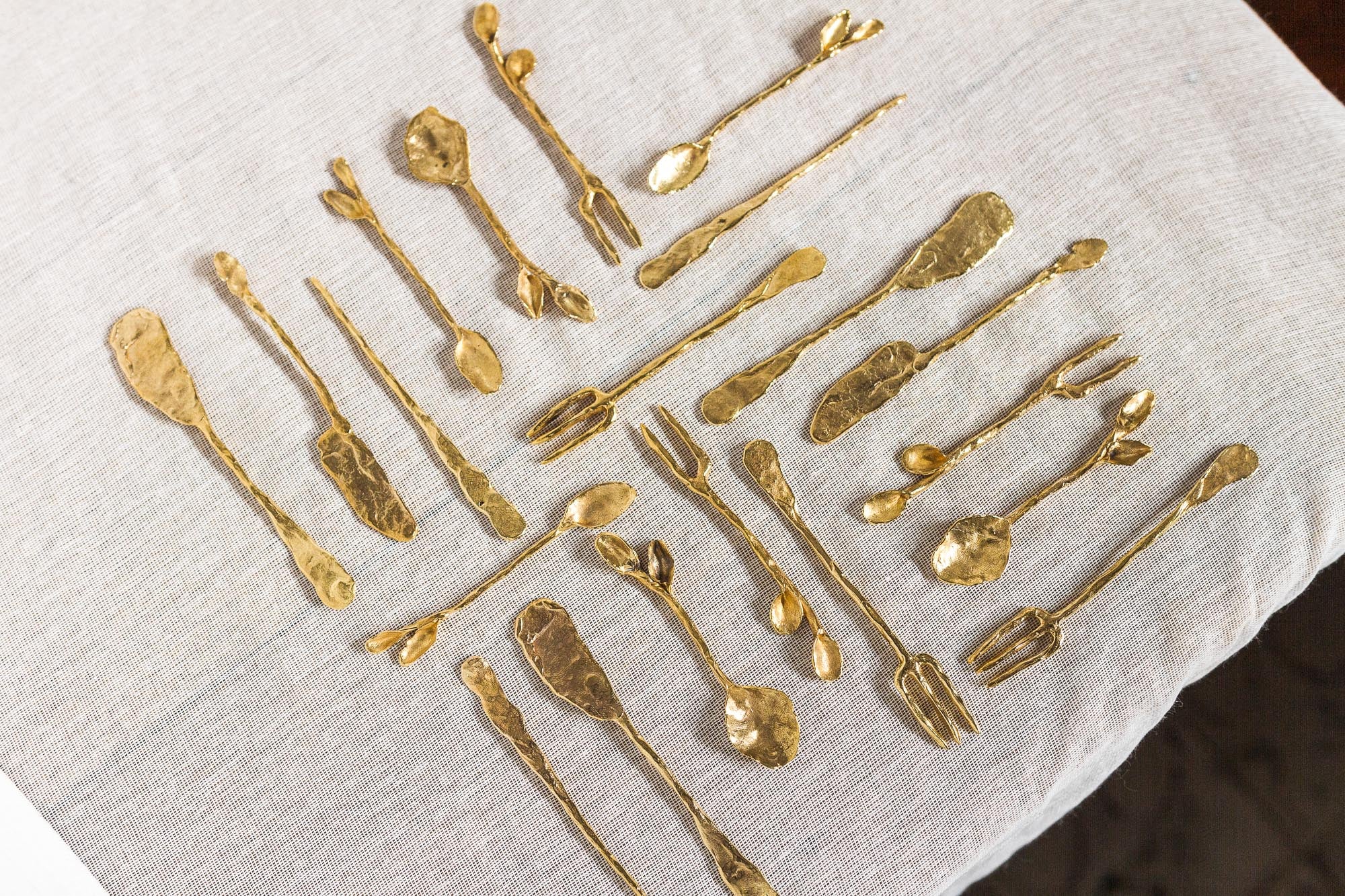 Handcrafted solid bronze utensils with organic shapes and textured finishes, artistically arranged on a light linen surface.