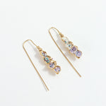 Aretes Azahar en bronce bañado en oro con detalles lavanda, diseño orgánico y alargado sobre fondo blanco.