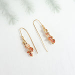 Aretes Azahar en tonos rojos sobre un fondo claro con ramas difuminadas de estilo botánico.