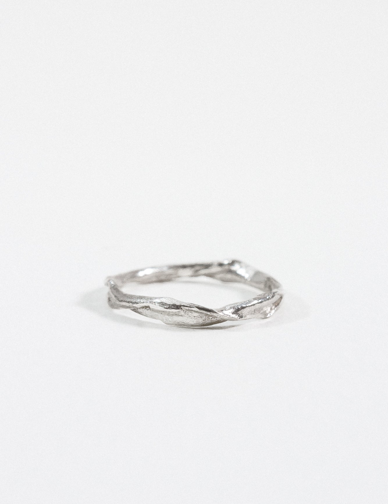 Anillo Nido Incrustado en plata esterlina con pequeño diamante de laboratorio incrustado en una banda orgánica retorcida, sobre fondo blanco.