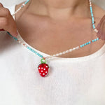 Primer plano del cuello de una niña con blusa blanca, mostrando el Collar Fresa con su colgante de fresa de vidrio rojo en el centro